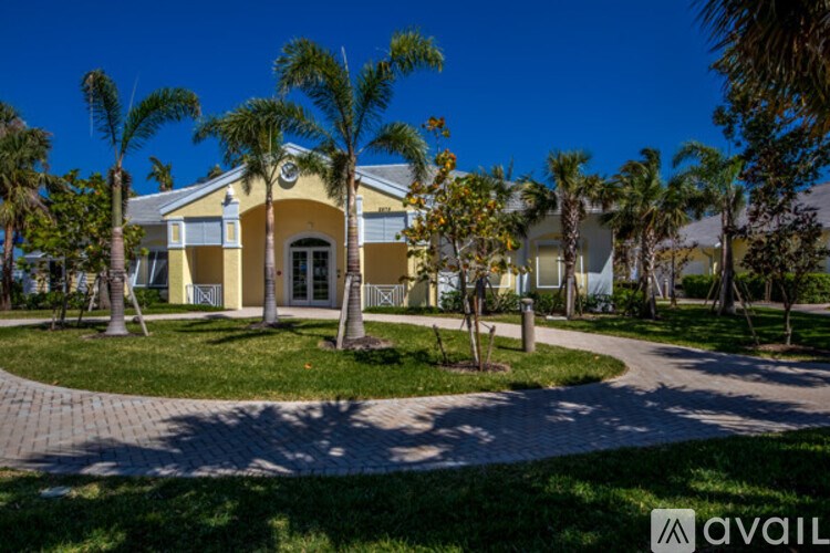 A yellow house with a white door and windows is surrounded by palm trees.