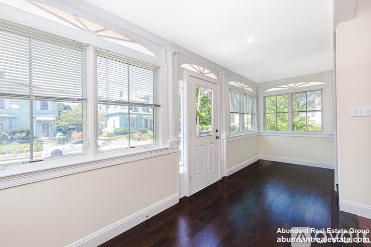 A room with white walls and wooden floors, with a view of a street outside the window.