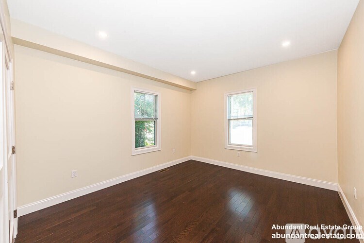 A spacious room with wooden floors and two windows.