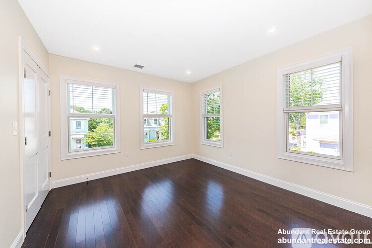 A spacious room with wooden floors and three windows.