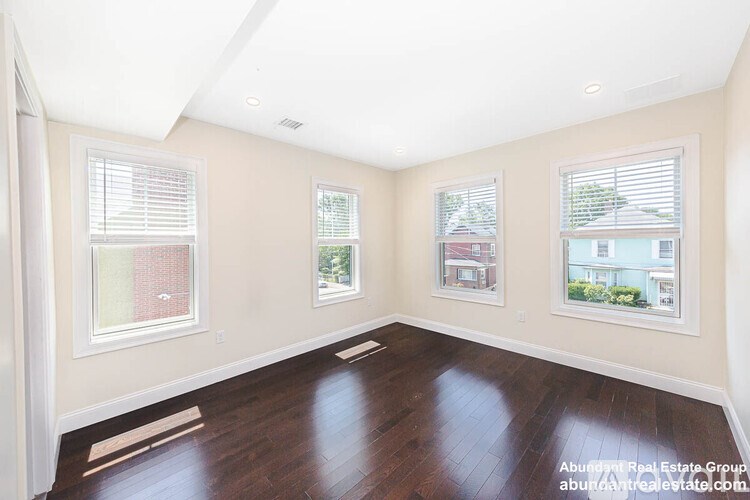 A spacious room with hardwood floors and three windows.