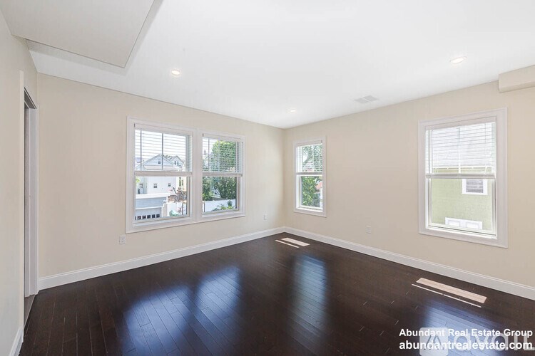 A spacious room with wooden floors and three windows.
