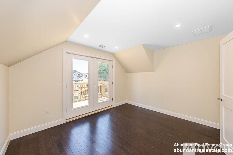 A room with a wooden floor and a slanted ceiling with a door leading outside.