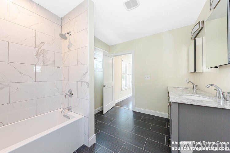 A bathroom with a white tub and marble tiles.