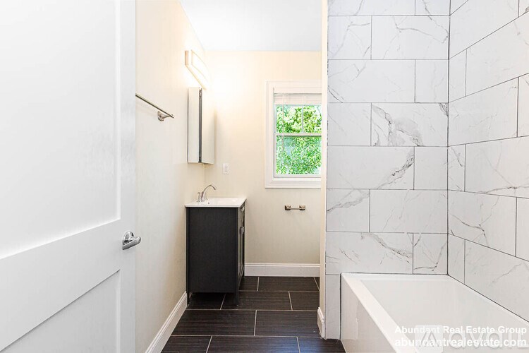 A bathroom with a white tub, a black cabinet, and a window with a green plant in it.