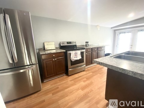 A kitchen with a stainless steel refrigerator, wooden cabinets, and a stove top oven.