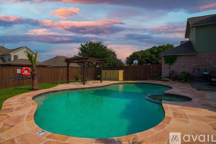 A pool surrounded by a stone patio and a wooden fence.