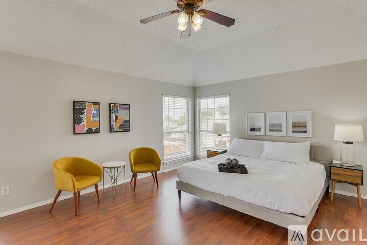 A bedroom with a bed, two chairs, and a ceiling fan.