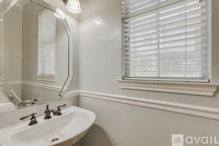 A white bathroom with a sink, mirror, and window with blinds.