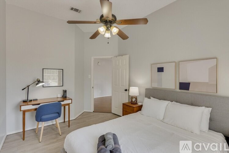 A bedroom with a bed, desk, and ceiling fan.