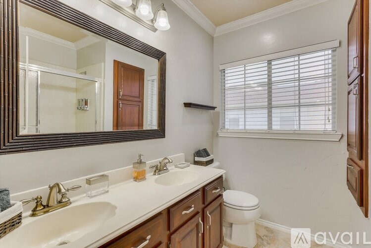 A bathroom with a mirror, sink, toilet, and window.