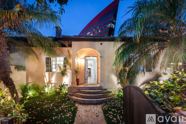 A house with a red roof and a front door is surrounded by plants and trees.