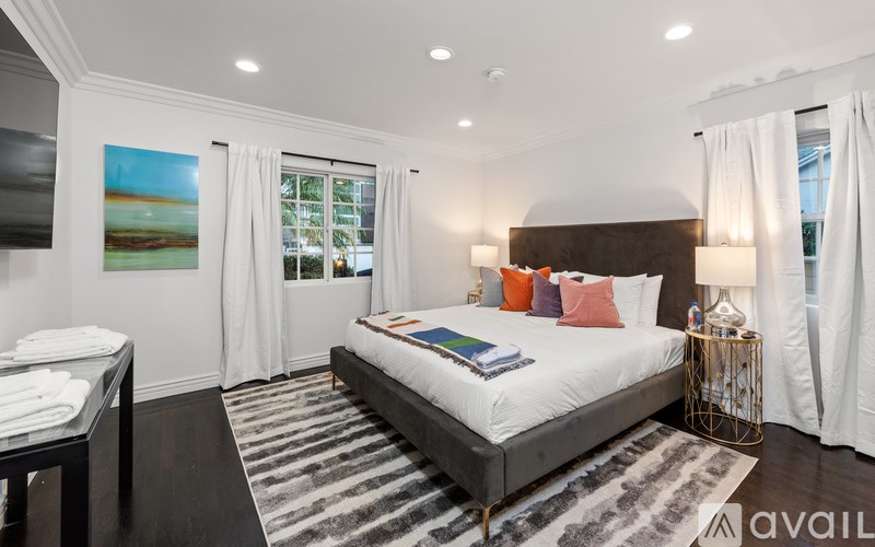 A bedroom with a large bed, a painting on the wall, and a striped rug on the floor.