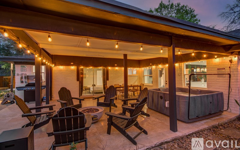 A patio with chairs and a hot tub under a roof with lights.