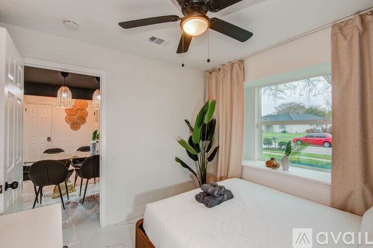 A bedroom with a bed, a ceiling fan, and a dining area in the background.
