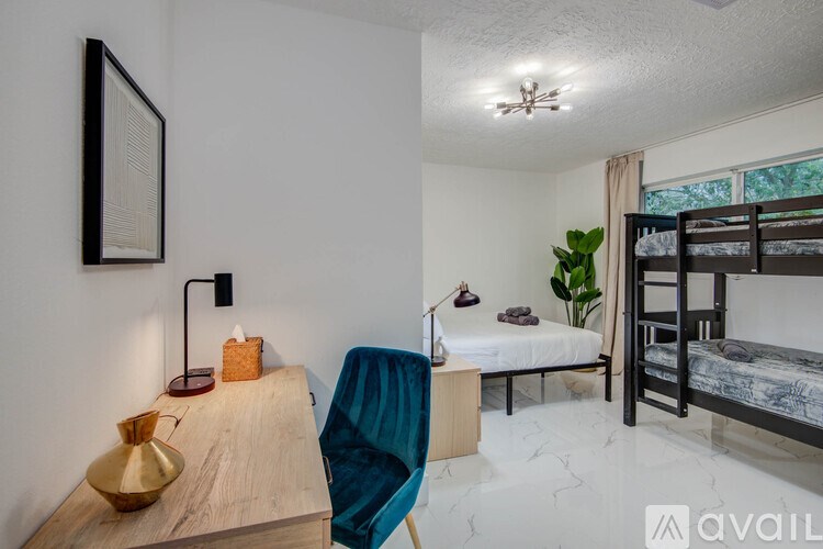 A room with a bunk bed, a chair, and a table with a lamp and a vase on it.