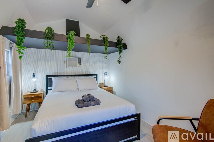 A bedroom with a bed, chair, and hanging plants.