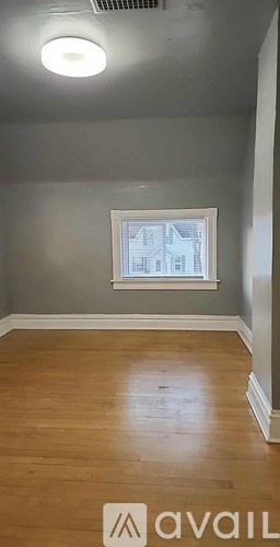 A room with wooden flooring and a window showing a building outside.
