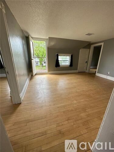 A room with wooden flooring and a window with a view of greenery outside.