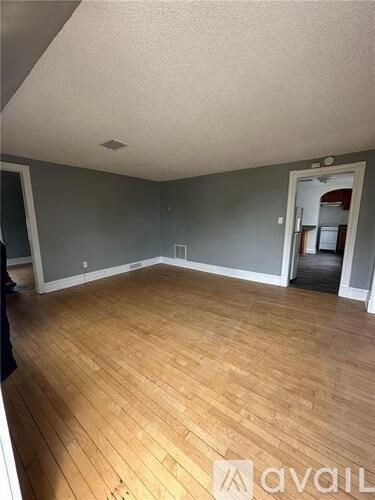 A room with wooden flooring and a doorway leading to another room.