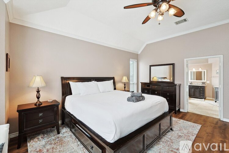 A bedroom with a large bed, a ceiling fan, and a dresser with a mirror.