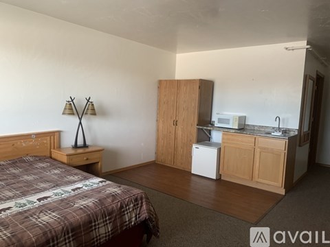 A bedroom with a bed, a nightstand with a lamp, and a small kitchenette.