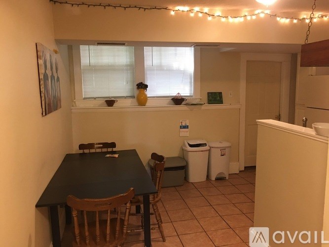 A kitchen with a table and chairs in the foreground and a window with blinds in the background.