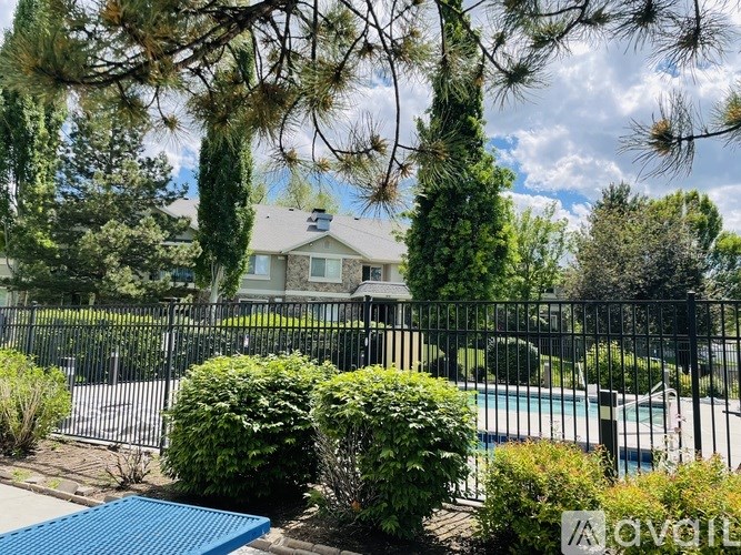 A house with a pool surrounded by a black fence and green bushes.