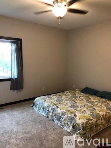 A bedroom with a bed, a ceiling fan, and a window with a curtain.