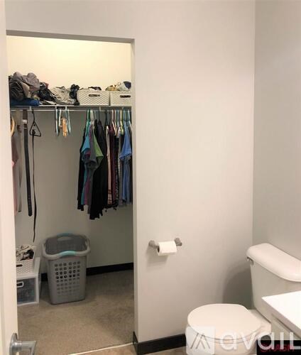 A small closet with clothes hanging and a white toilet.