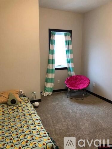 A bedroom with a bed, a chair, and a window with striped curtains.