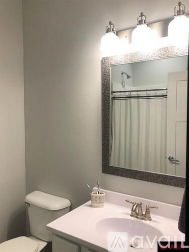 A bathroom with a toilet, sink, mirror and lights.