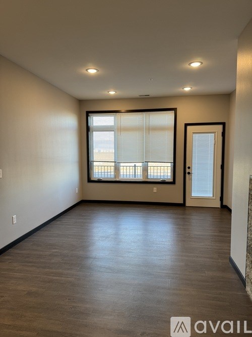 A spacious room with wooden flooring and a large window with blinds.