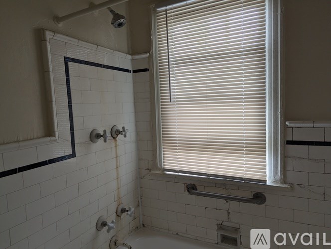 A bathroom with a shower, a window with blinds, and a sign that says "AVAIL".