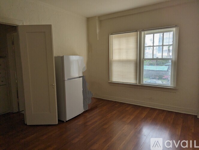 A room with a fridge and a window with blinds.