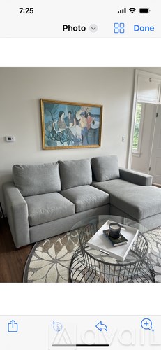 A grey couch sits in a living room with a painting on the wall above it.