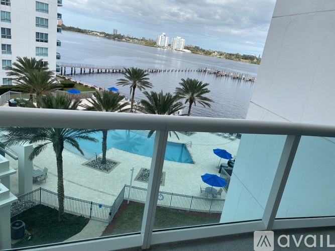A balcony with a pool and palm trees overlooks a body of water.