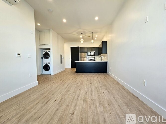 A spacious room with wooden flooring and a kitchen area in the background.