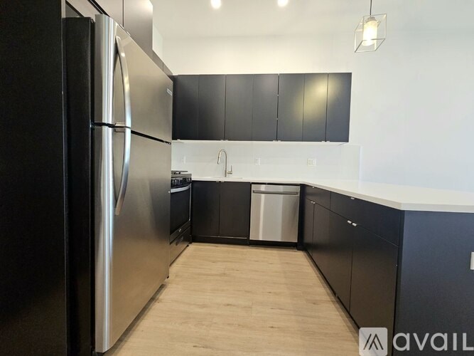 A kitchen with a refrigerator, cabinets, and a trash can.