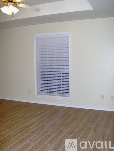 A room with a window covered by white blinds and wooden flooring.