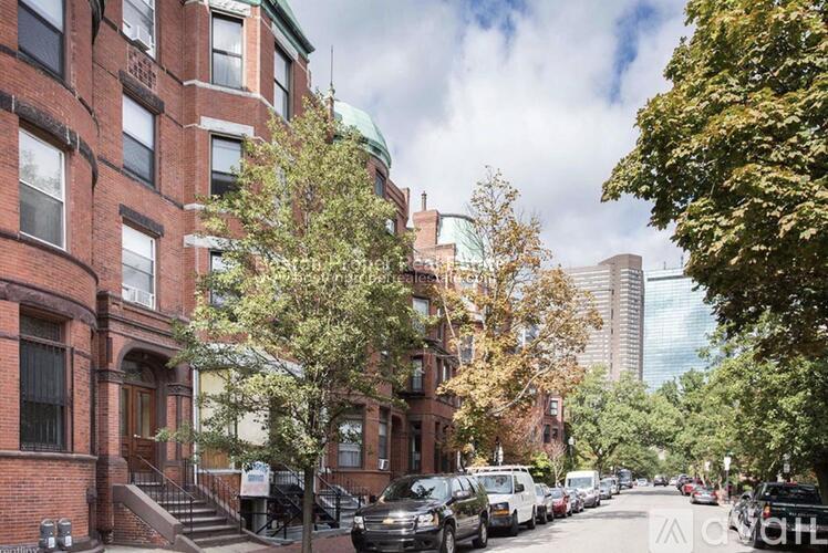 A street view of a row of red brick buildings with cars parked on the side.