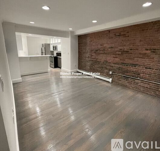 A spacious room with wooden flooring and a brick wall.