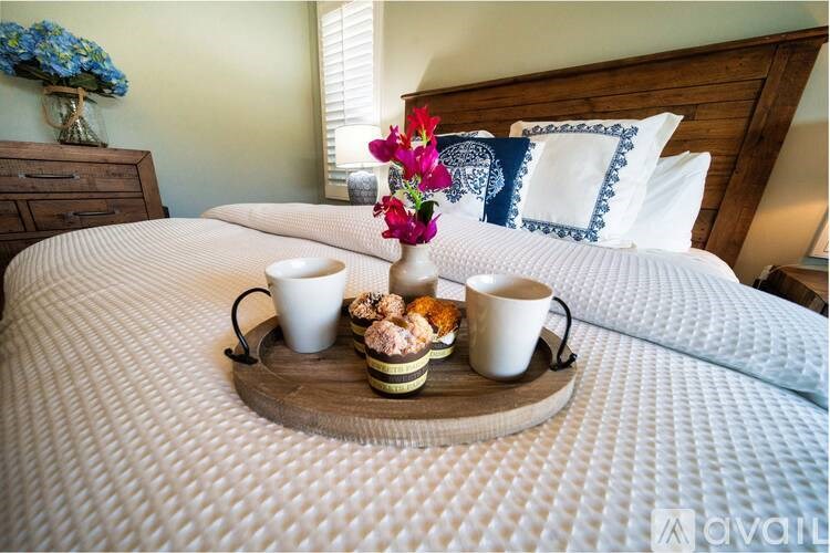 A tray with two cups and a bowl of cookies is on a bed.