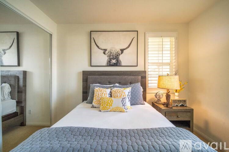 A bedroom with a bed, a nightstand with a lamp, and a painting of a bull's head on the wall.