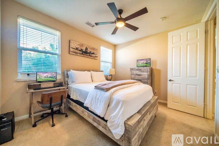 A bedroom with a bed, desk, and a ceiling fan.