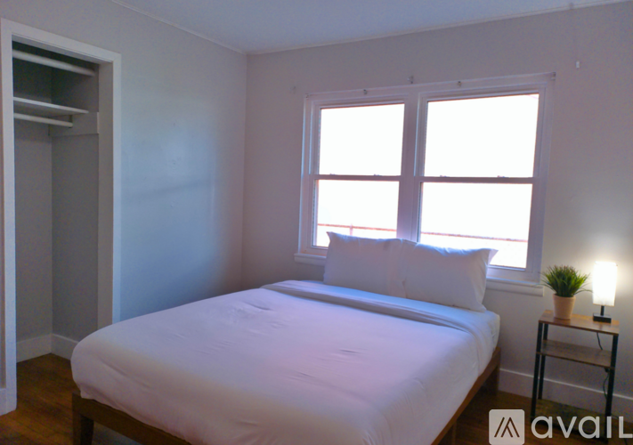 A bedroom with a bed, a small table with a lamp, and a window.
