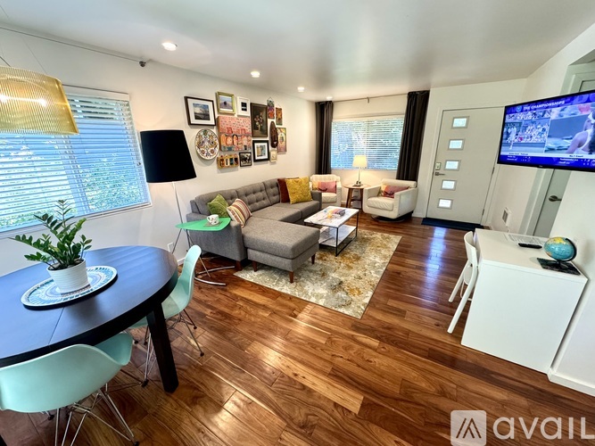 A living room with a round table and chairs, a sofa, a TV, and a window with blinds.