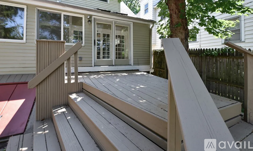 A wooden deck with a bench and a tree in front of a house.