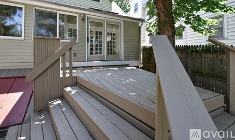 A wooden deck with a bench and a tree in front of a house.