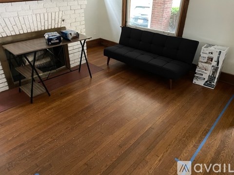 A black sofa sits in a room with wooden floors and a brick wall.